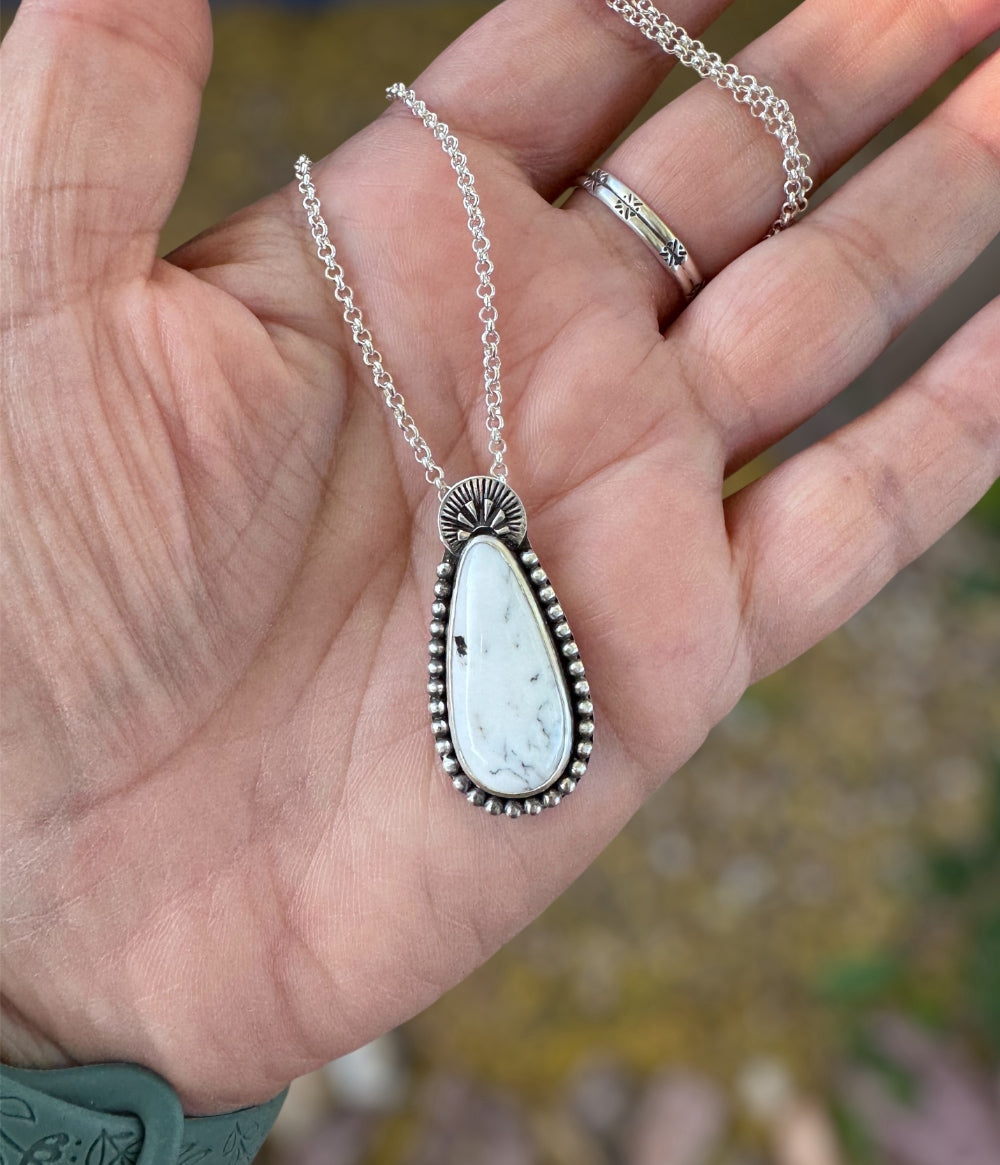 A handmade sterling silver necklace with a white buffalo teardrop shaped stone wrapped in sterling silver beaded balls and handstamped at the top.