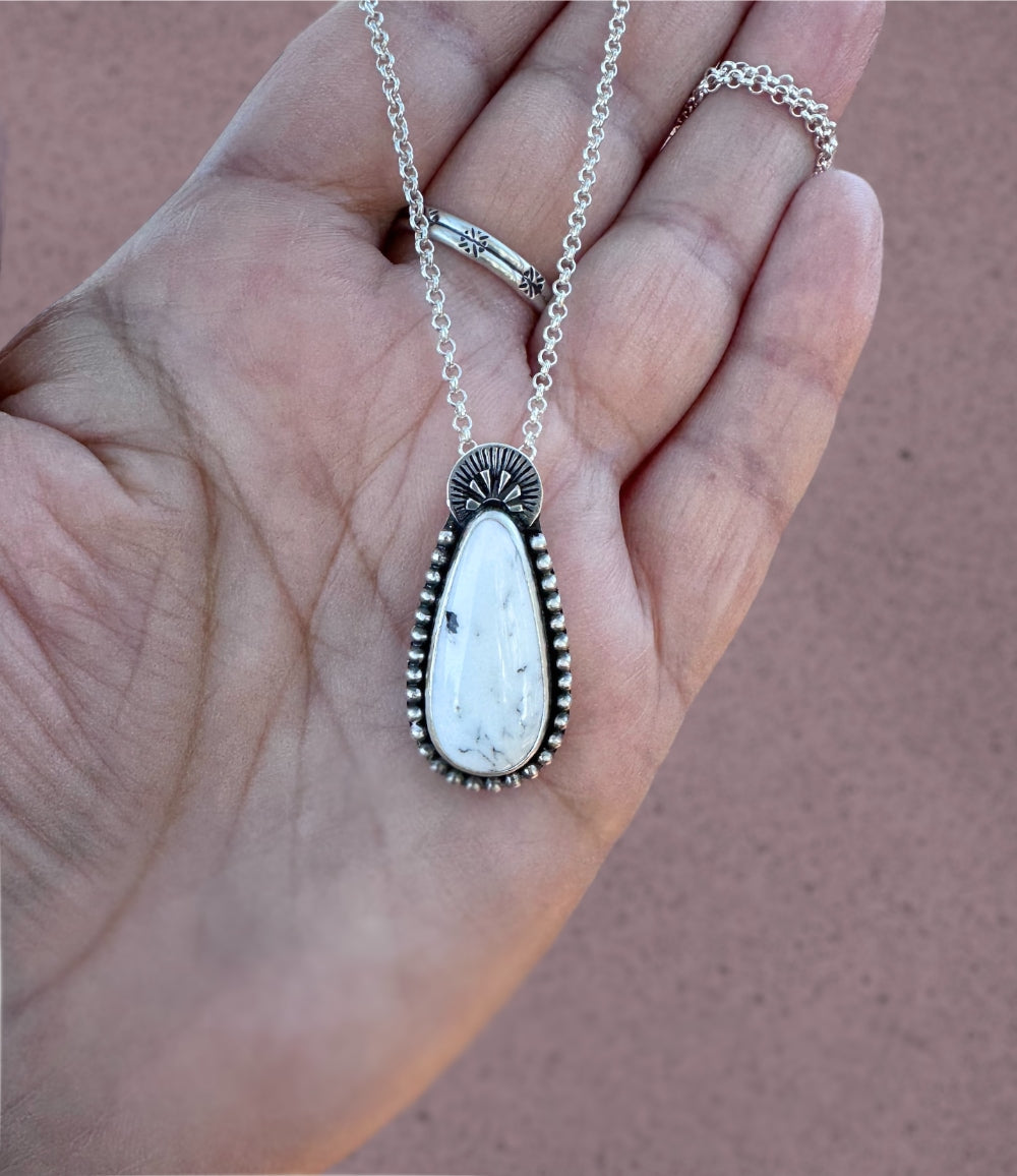 A handmade sterling silver necklace with a white buffalo teardrop shaped stone wrapped in sterling silver beaded balls and handstamped at the top.