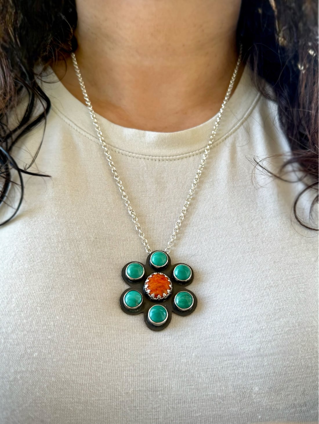 A coral and turquoise stone flower shaped handmade sterling silver necklace worn.