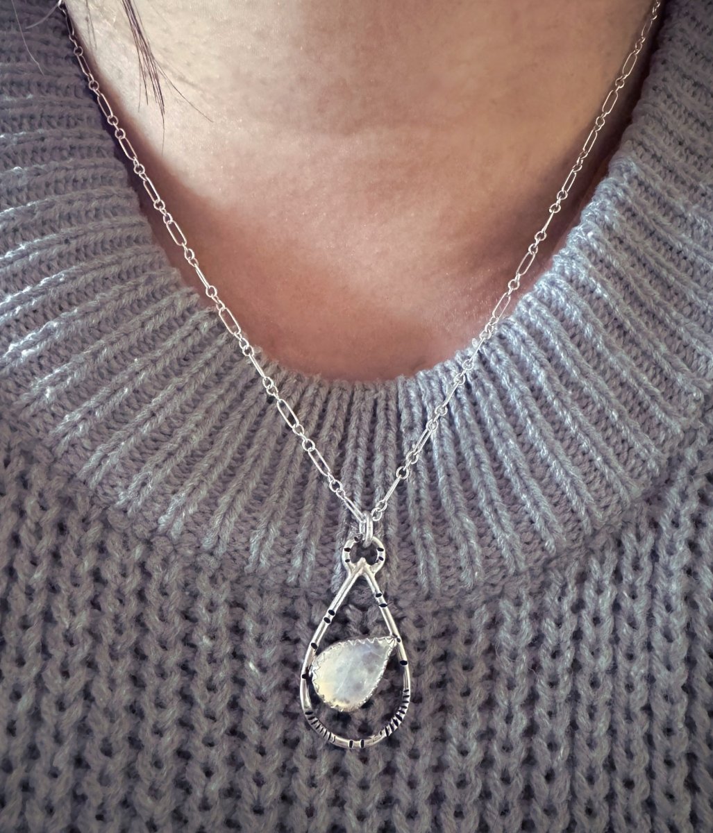Silver necklace with a pendant worn on a textured sweater.