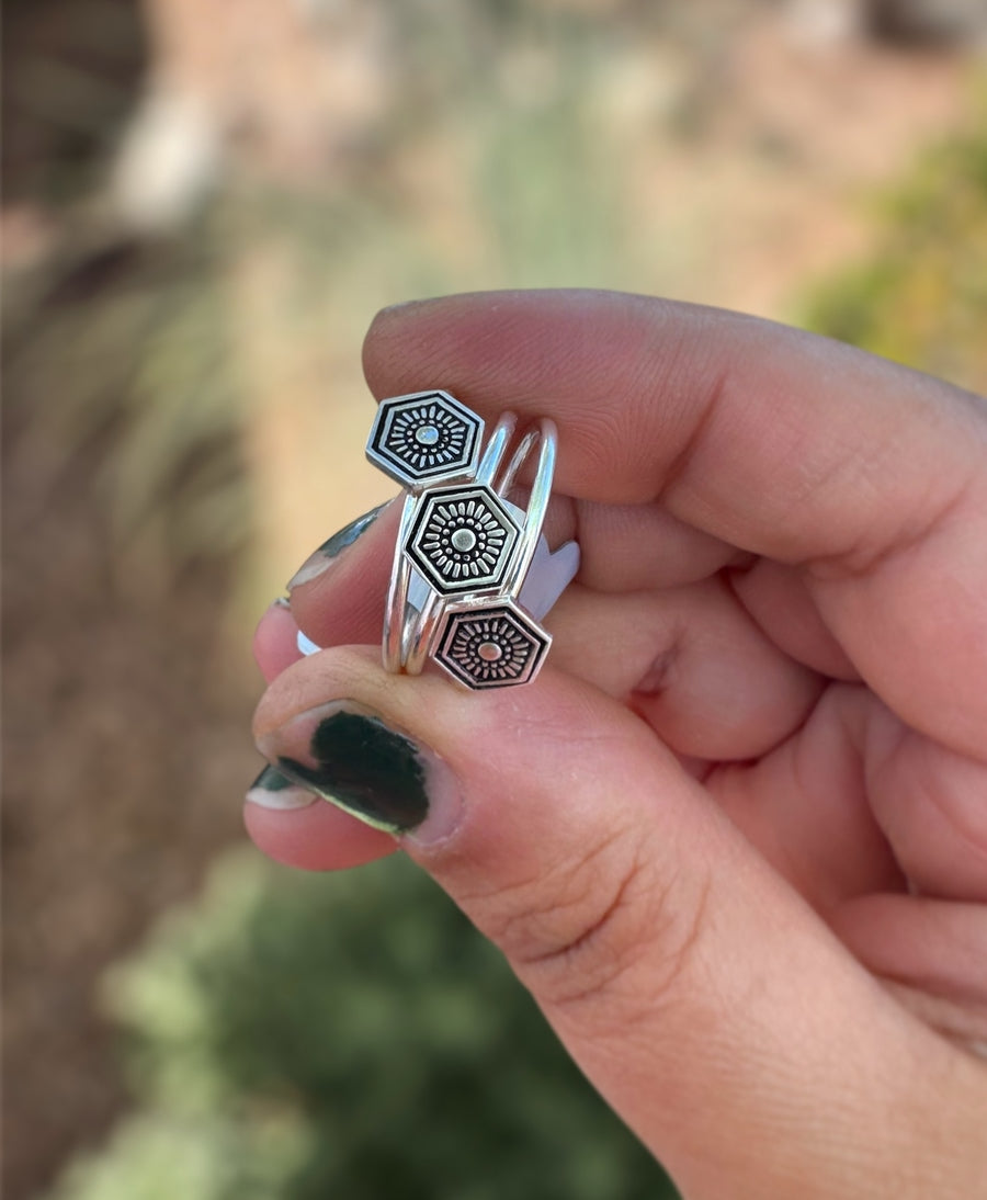 Three handmade rings, held in hand, stamped hexagon shaped soldered onto a round ring band.