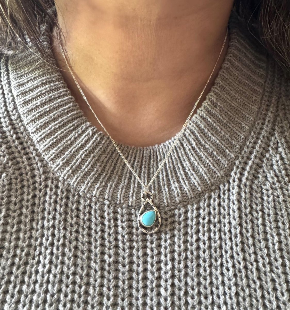 Necklace with a turquoise pendant worn by a person in a gray sweater.