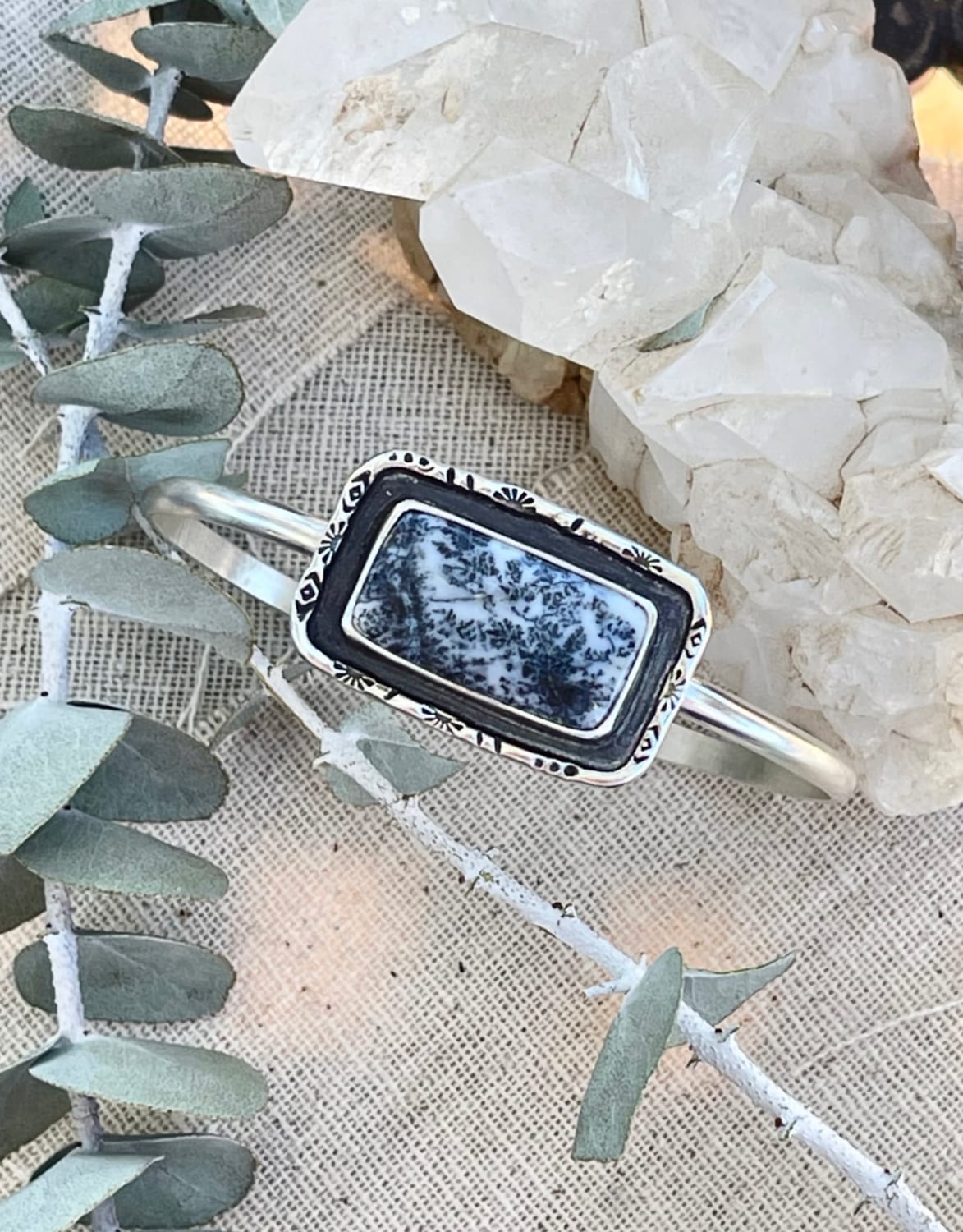 a rectangular shaped dendritic agate stone, with hand stamped wire details around it, on a sterling silver cuff