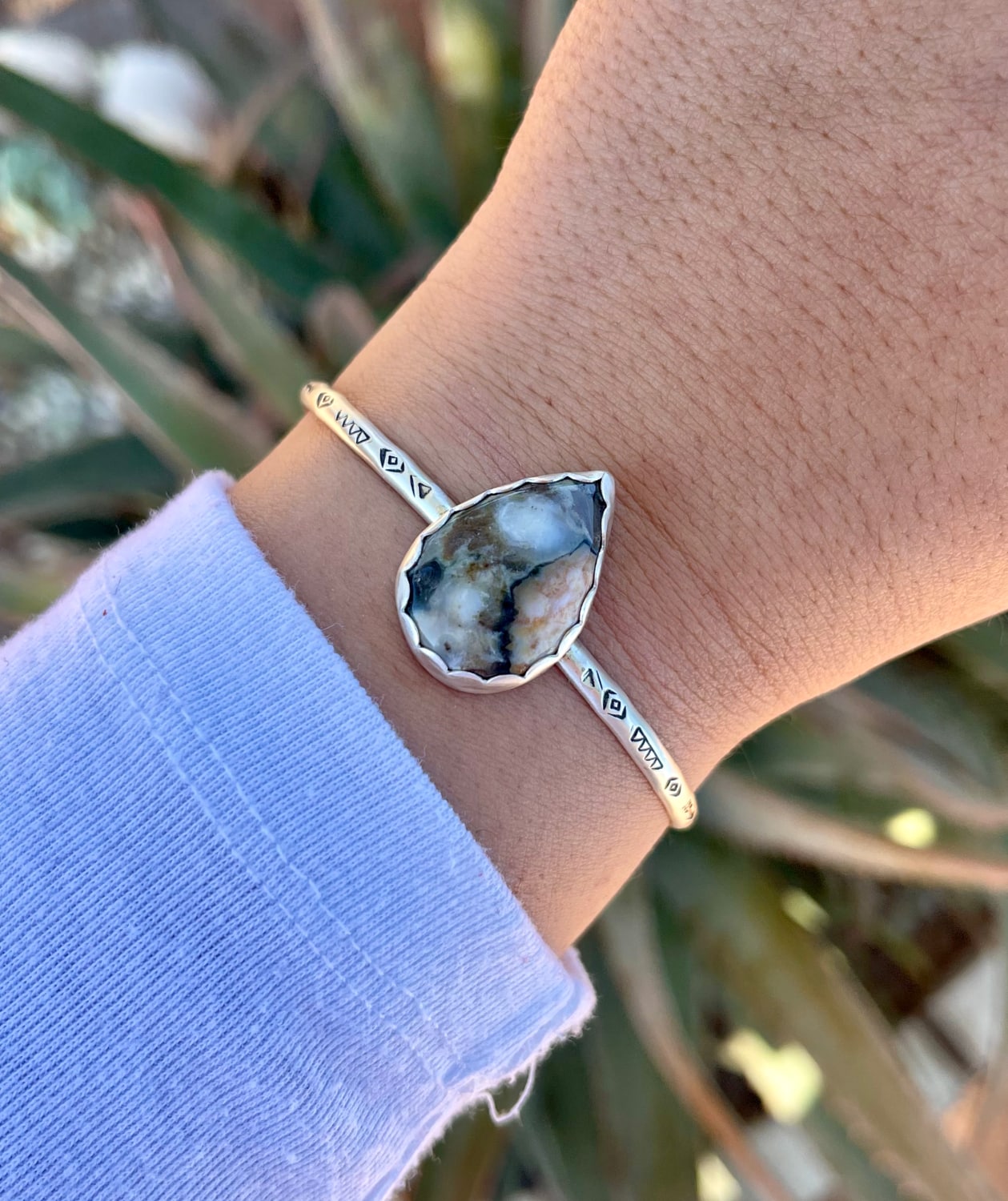 sterling silver handstamped cuff bracelet with a big teardrop shaped jasper stone in a scalloped edge bezel shown on wrist