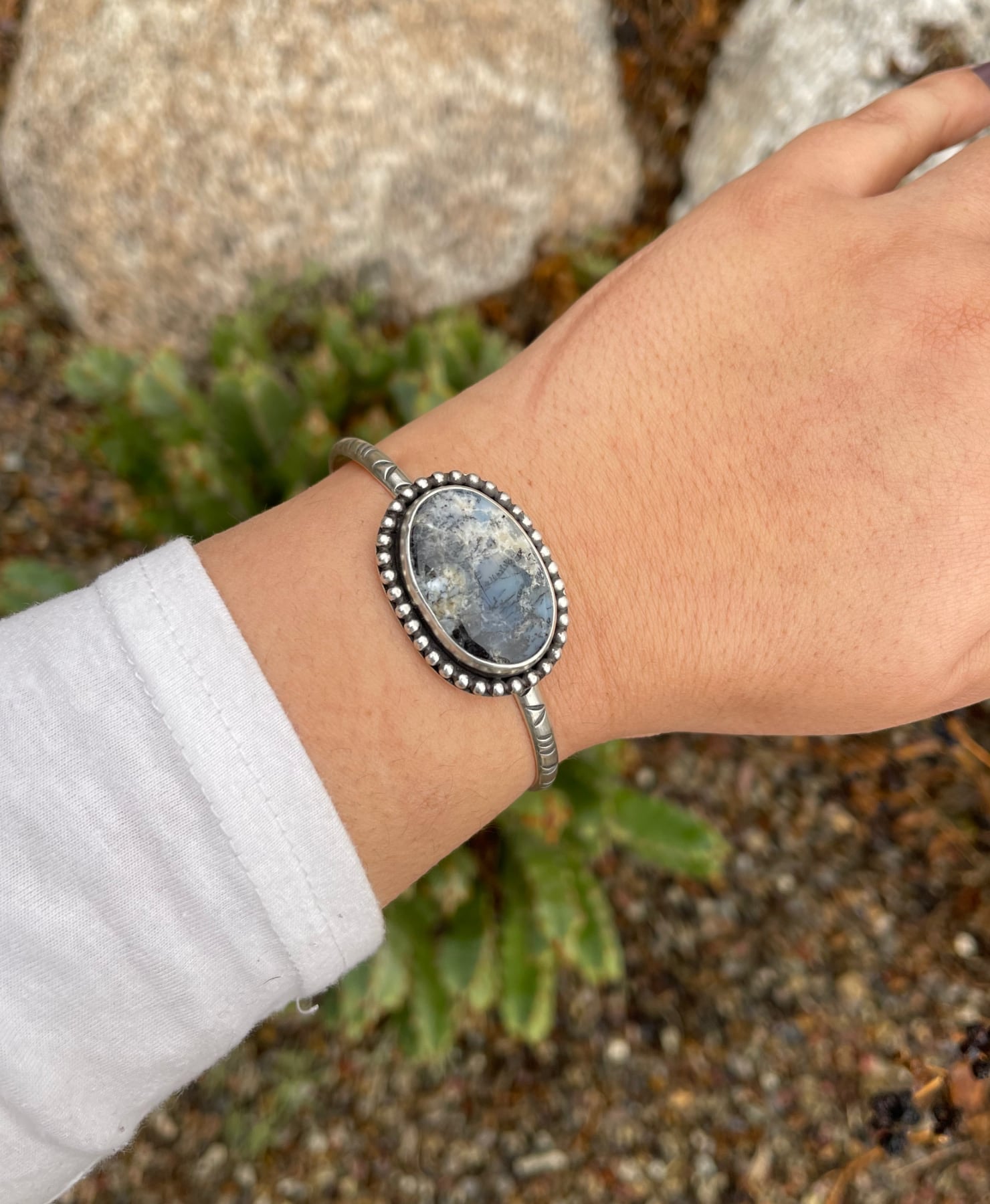 handstamped sterling silver cuff bracelet with a round dendritic opal stone with sterling bead wire around it shown on wrist