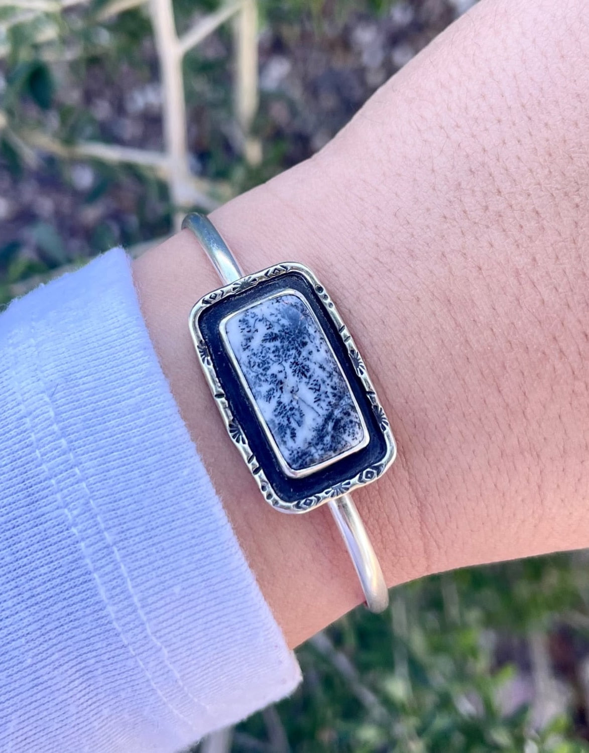 sterling silver cuff bracelet with a rectangle shaped black and white dendritic agate stone with hand stamped sterling wire border shown on wrist